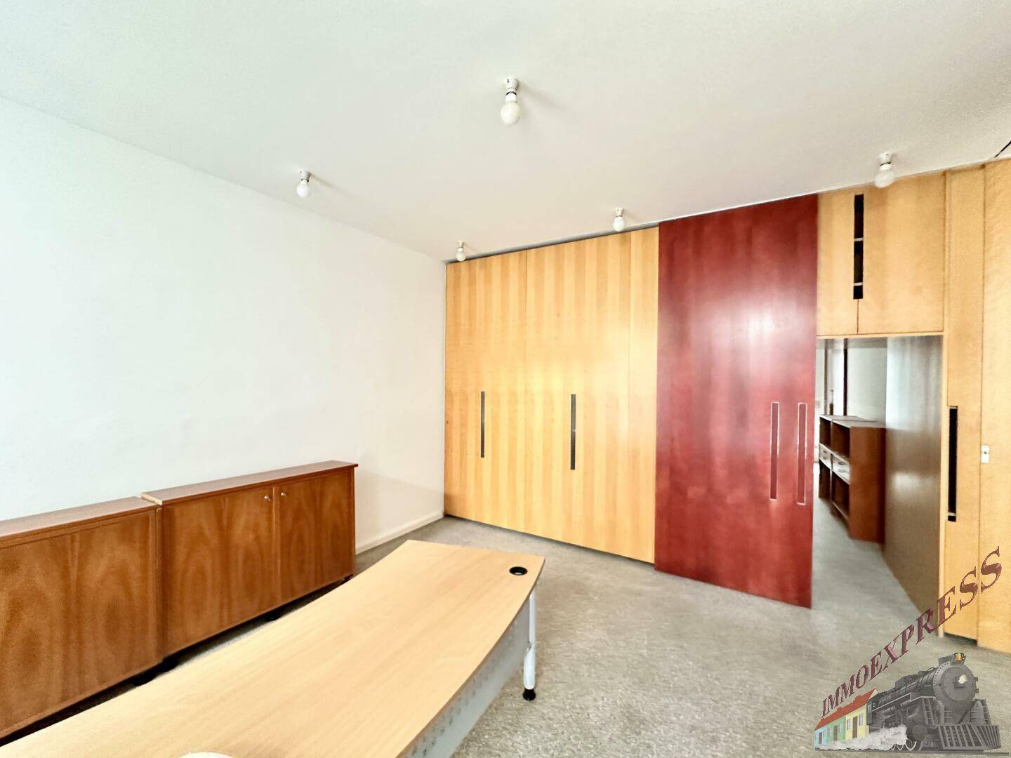 Büroraum mit einer Wand aus Holzschränken und einer roten Schiebetür, bietet flexible Raumnutzung.