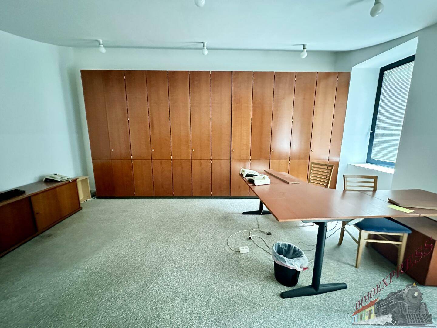 Büroraum mit einer langen Wand aus Holzschränken und einem großen Tisch, bietet viel Stauraum.