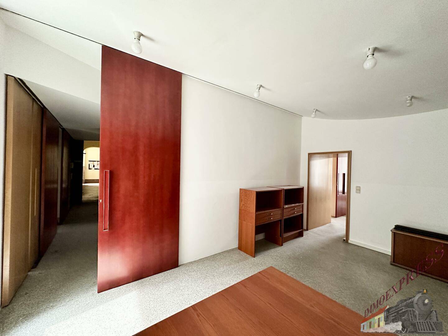 Büroraum mit einem Schreibtisch und einem Sideboard, ergänzt durch eine große rote Schiebetür.