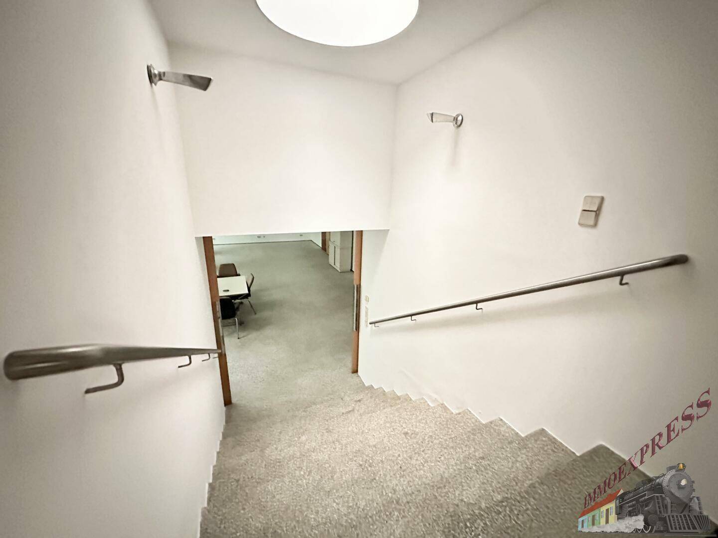 Heller Treppenaufgang mit Handläufen und Teppichboden, der zu einem unteren Bereich führt.