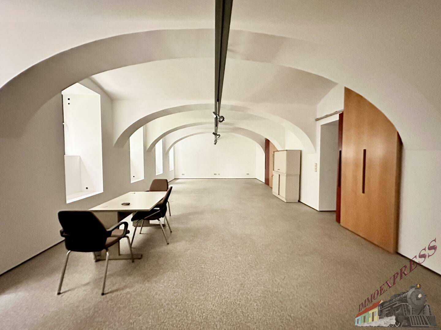 Großer, offener Bürobereich mit gewölbten Decken und Teppichboden, ausgestattet mit Tischen und Stühlen.