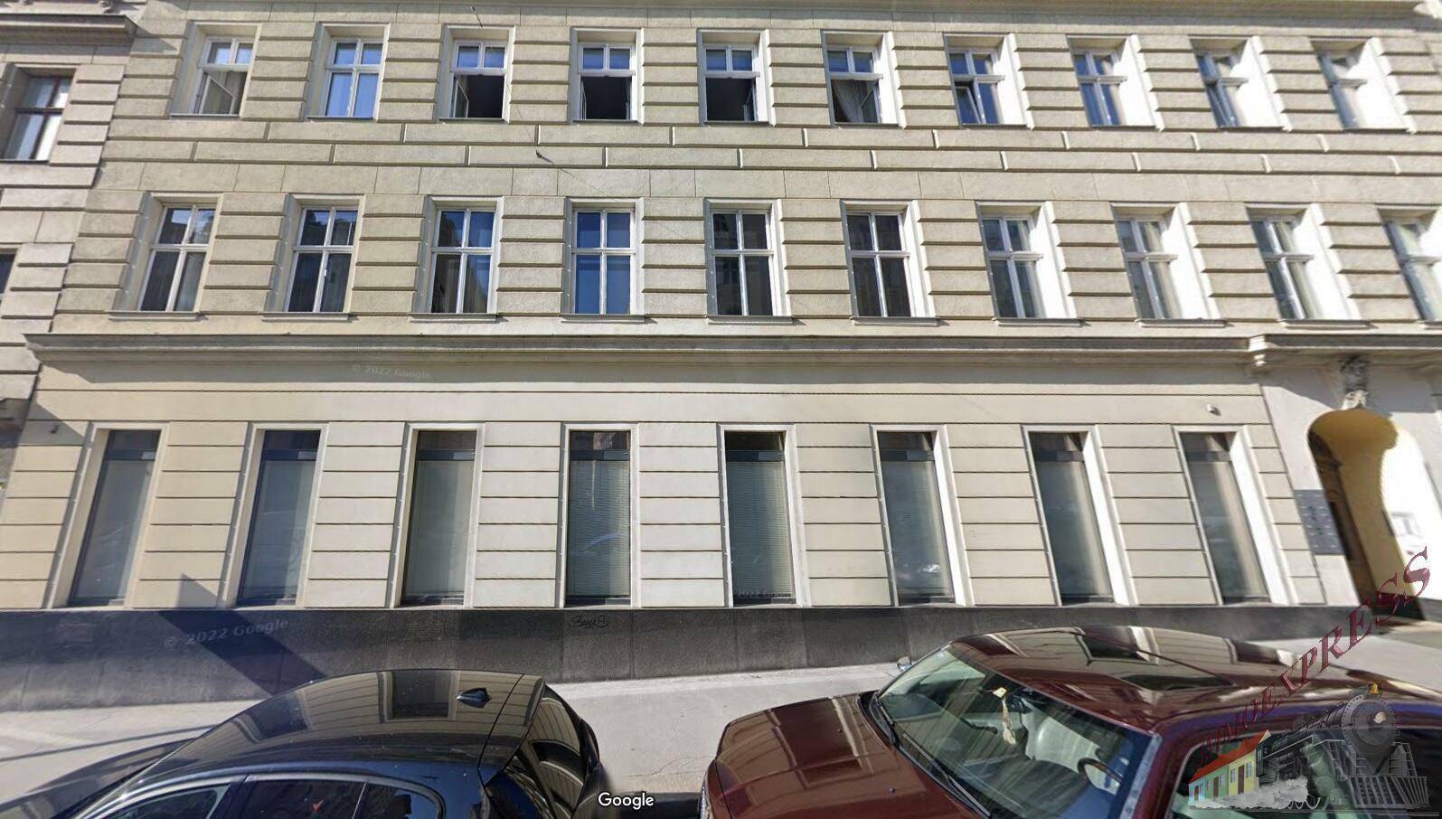Klassische Gebäudefassade mit vielen Fenstern und geparkten Autos davor, typisch für eine Stadtansicht.