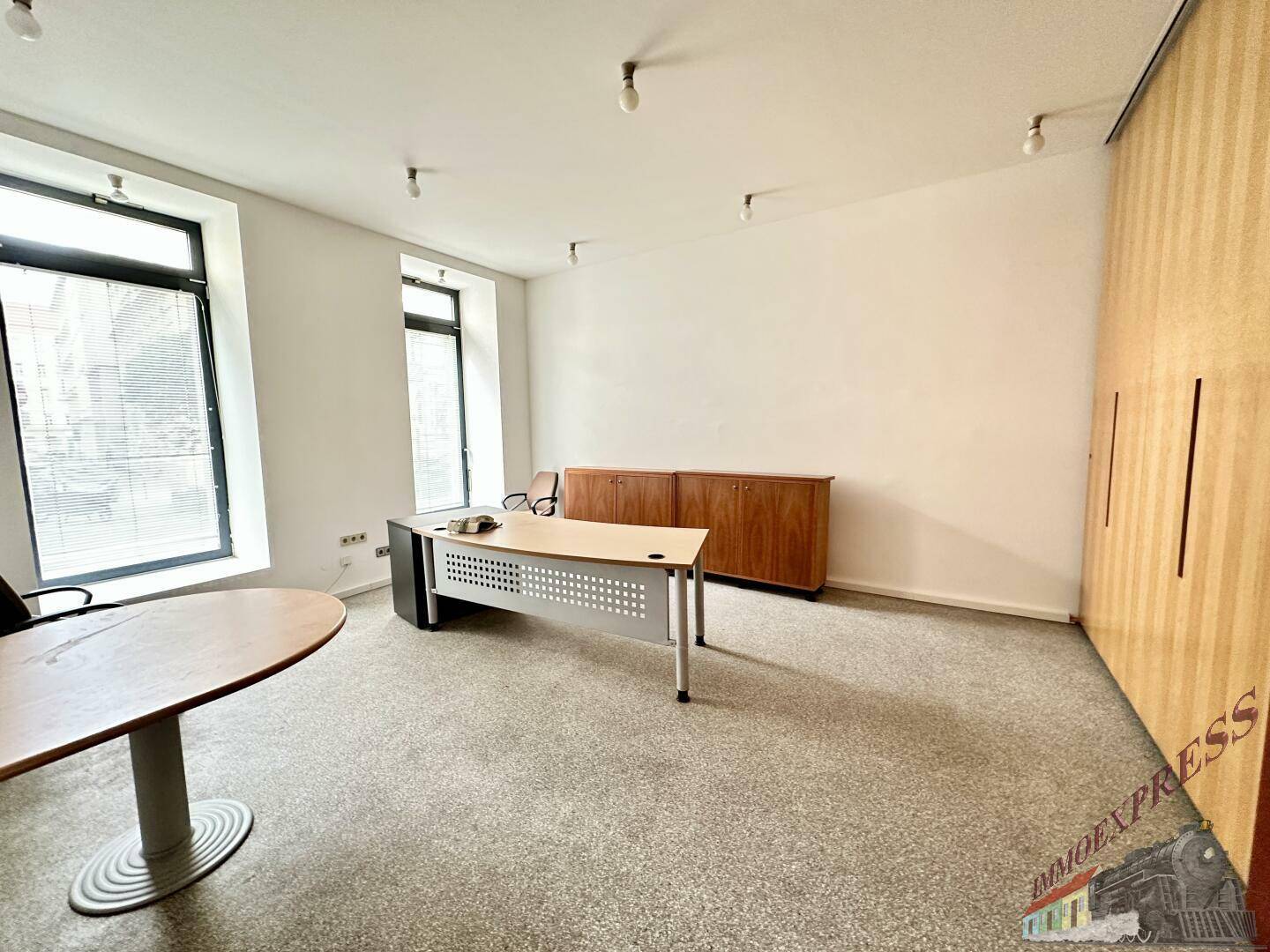 Büroraum mit einem Schreibtisch und einem Sideboard, ergänzt durch eine Wand mit Holzschränken.