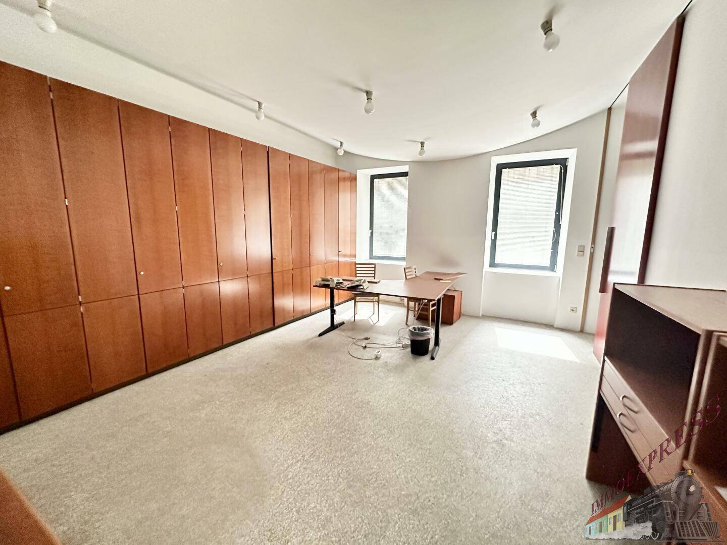 Büroraum mit einer langen Wand aus Holzschränken und zwei Fenstern, bietet viel Stauraum.