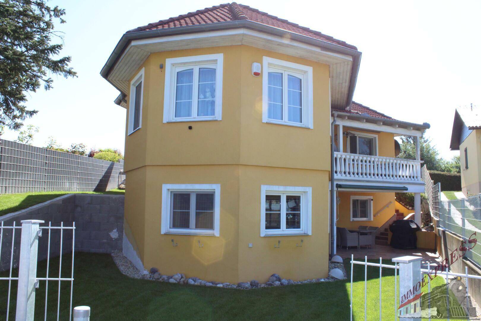 Seitenansicht des Hauses mit Balkon und einer überdachten Terrasse, ausgestattet mit Gartenmöbeln und Grill.
