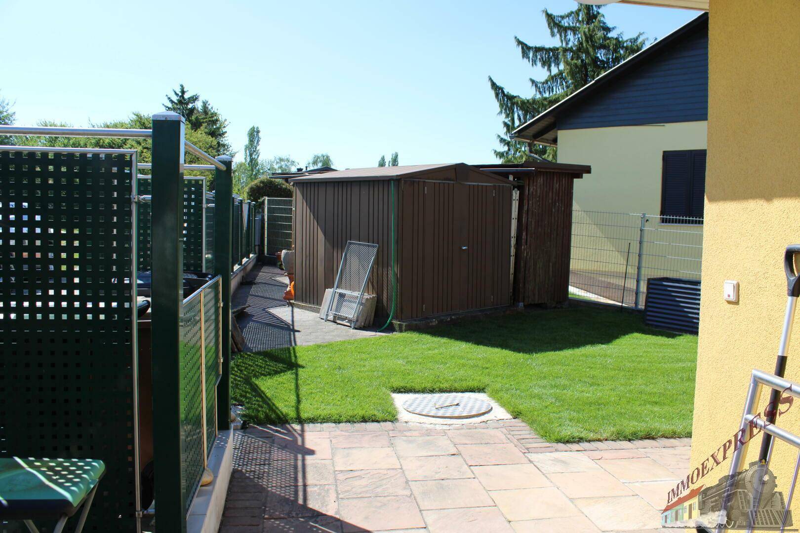 Gepflegter Garten mit Rasenfläche, gepflastertem Weg und einem braunen Gartenschuppen.