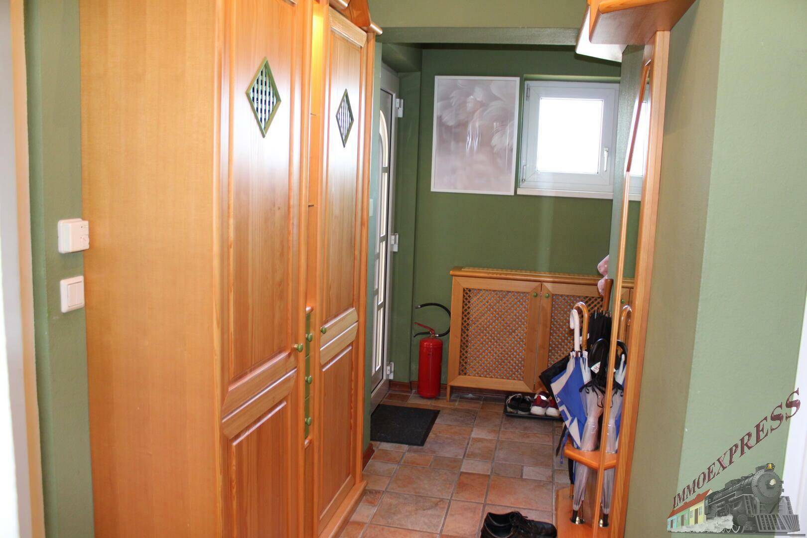 Eingangsbereich mit Fliesenboden, grünen Wänden und einem großen Holzschrank.