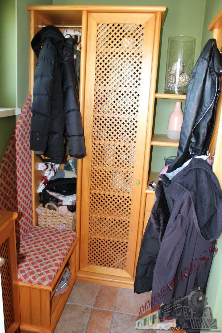 Eingangsbereich mit Garderobe, Holzschrank und Sitzbank in grüner Umgebung.