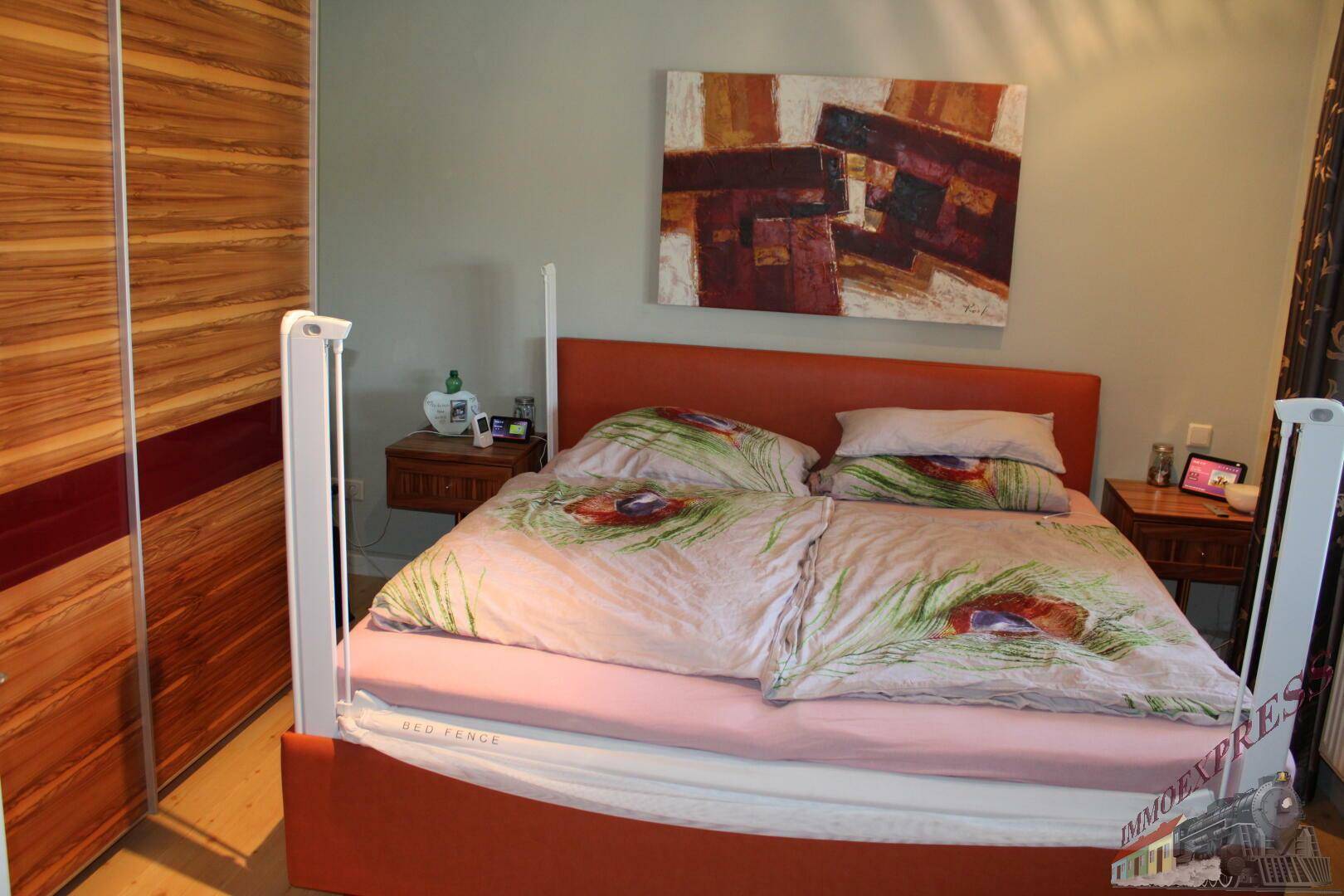 Schlafzimmer mit orangefarbenem Bett, Holzschrank und moderner Kunst an der Wand.