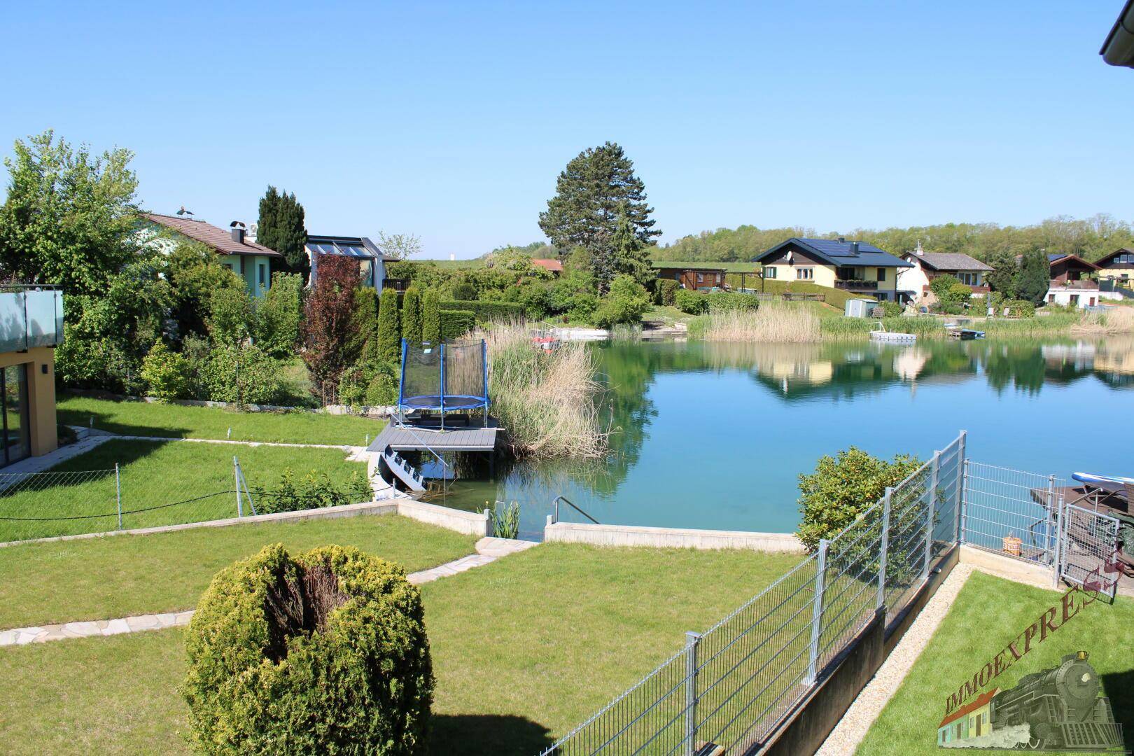 Gartenbereich mit Rasen und direktem Zugang zum See, inklusive Trampolin auf einem kleinen Steg.