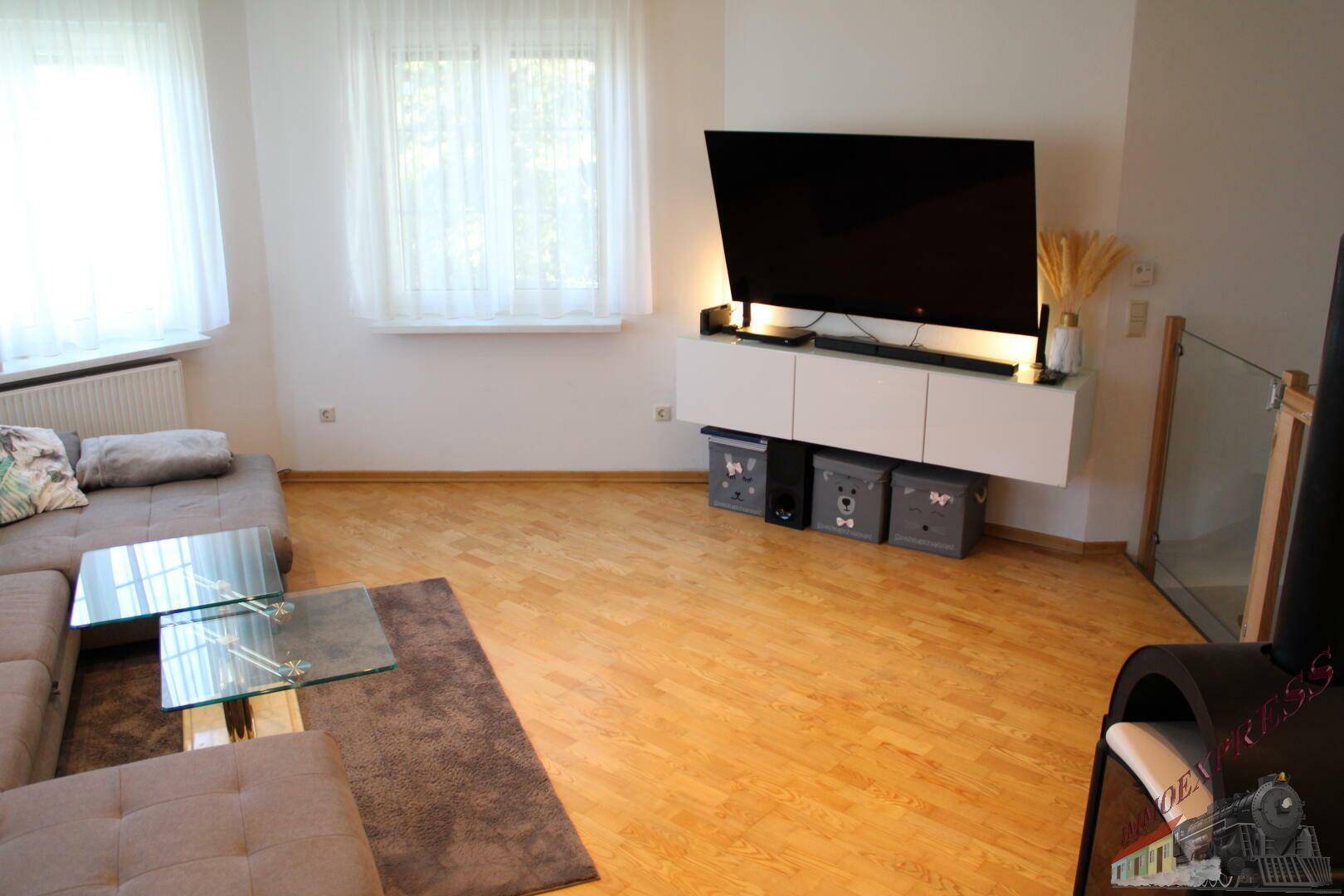 Wohnzimmer mit Holzboden, wandmontiertem Fernseher und einem bequemen Sofa.