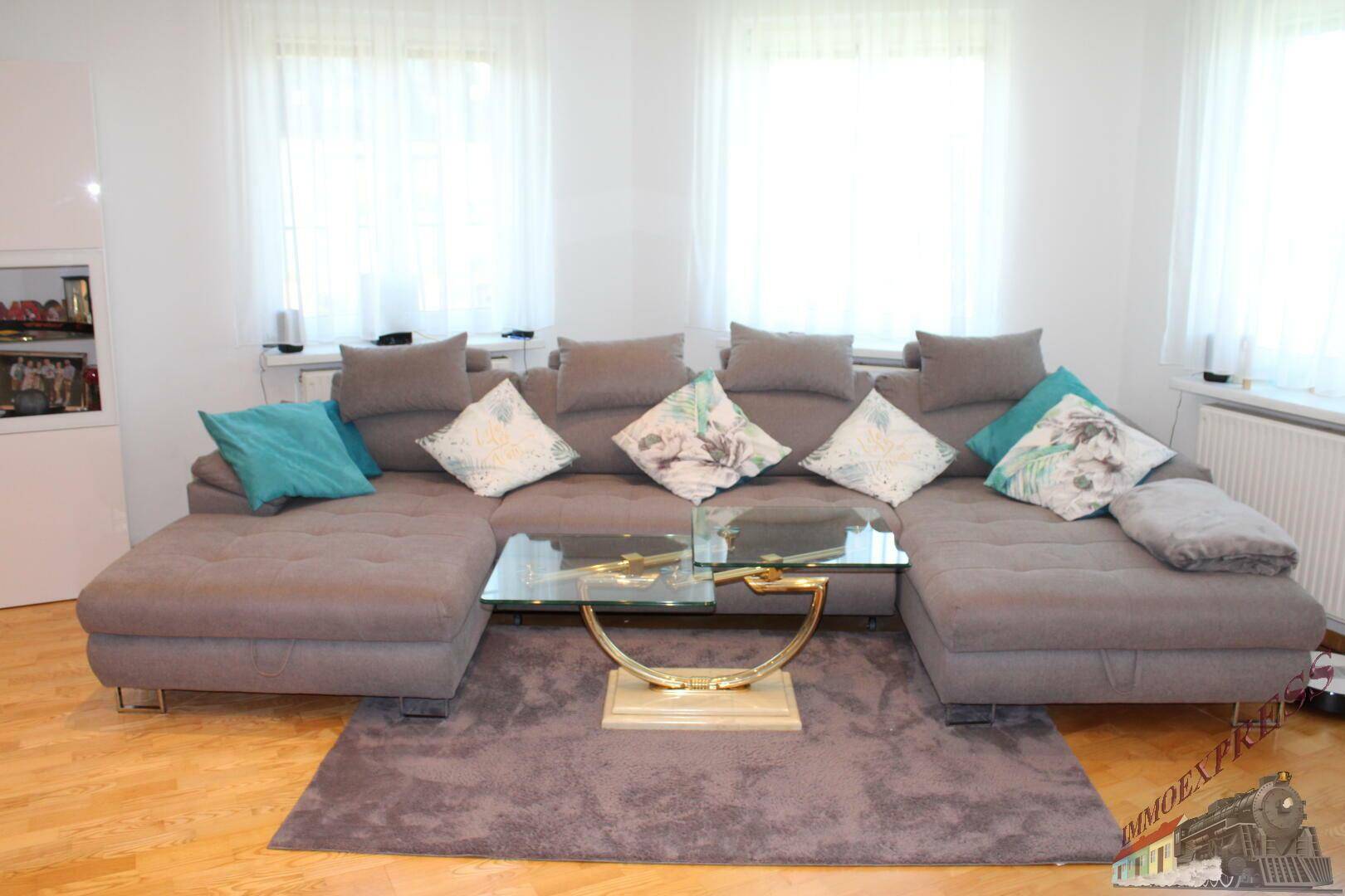 Gemütliches Wohnzimmer mit großem Ecksofa, Glastisch und hellem Parkettboden.