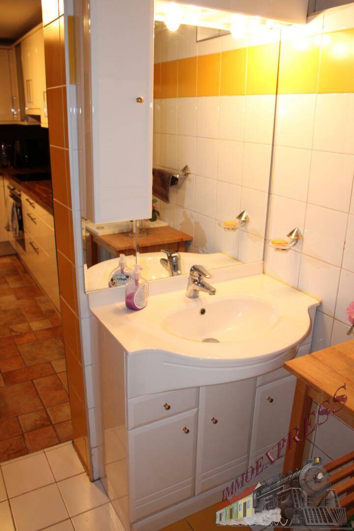 Kleines Badezimmer mit Waschbecken, Spiegelschrank und gelb-weißen Fliesen.