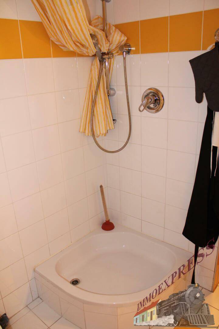 Kleine Dusche mit weißem Fliesenboden und gelb-weißem Duschvorhang.