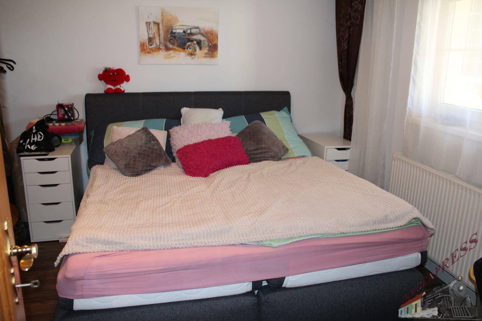 Schlafzimmer mit dunkelgrauem Bett, weißen Nachttischen und einem Fenster.