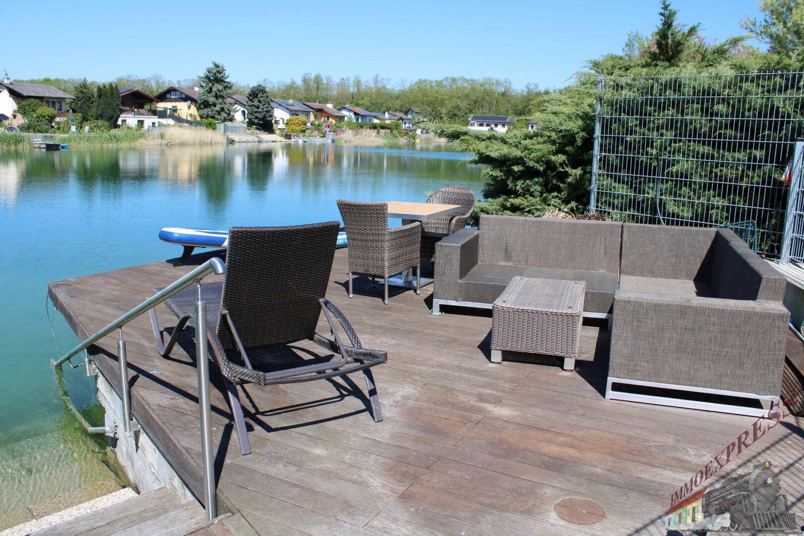 Holzterrasse direkt am Seeufer mit bequemen Lounge-Möbeln und Blick auf das Wasser.