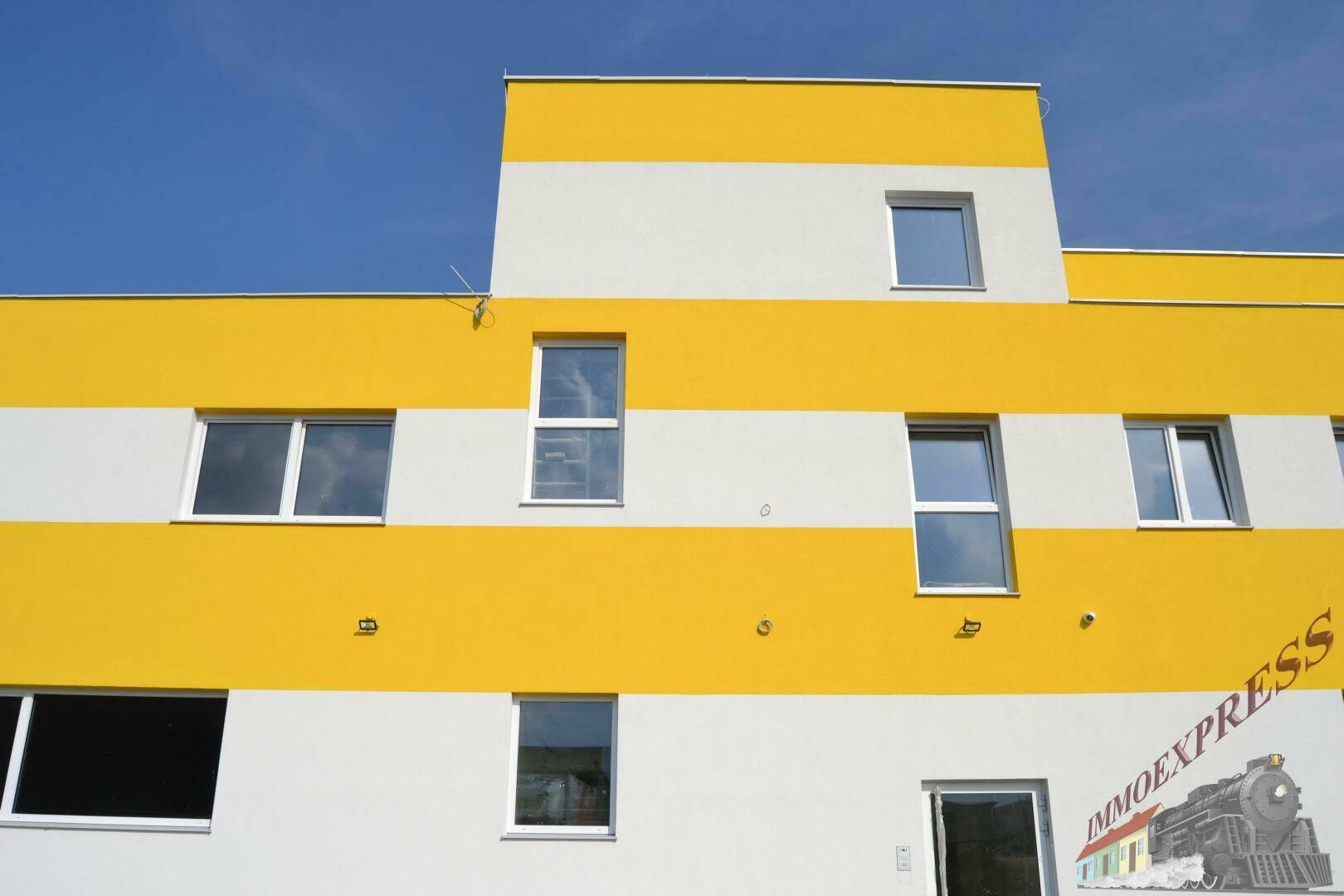 Moderne Gebäudefassade mit auffälligen gelben und weißen Streifen unter blauem Himmel.