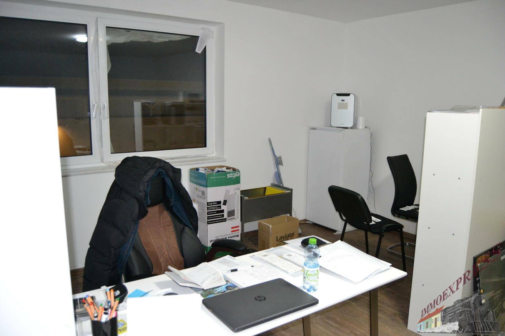 Arbeitsbereich in einem Büro mit Schreibtisch, Laptop und einem großen Fenster, das den Raum erhellt.