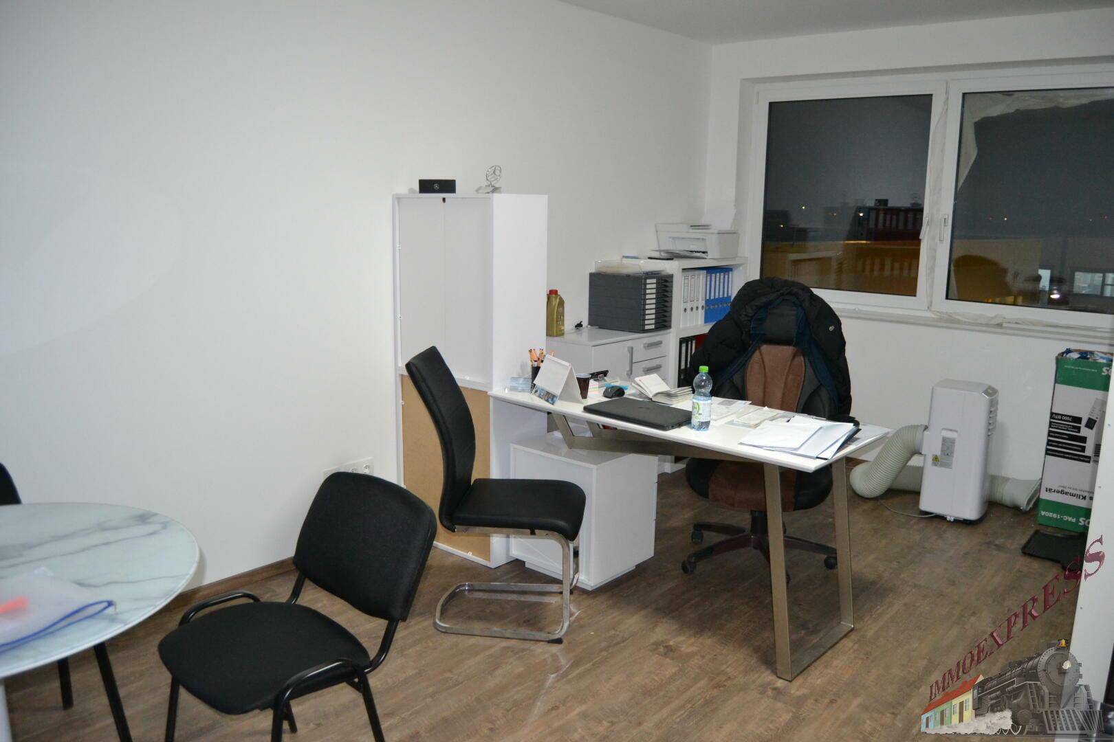 Geräumiges Büro mit Schreibtisch, mehreren Stühlen und einem großen Fenster, das Tageslicht hereinlässt.