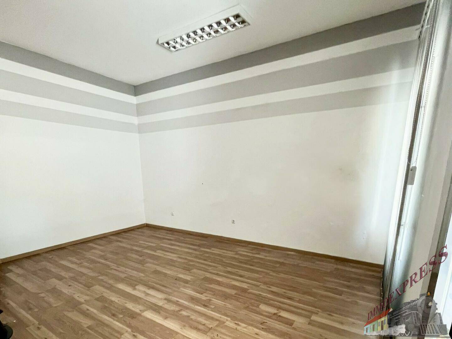 Leerer Büroraum mit Holzboden und weiß-grau gestreiften Wänden, bereit zur Einrichtung.