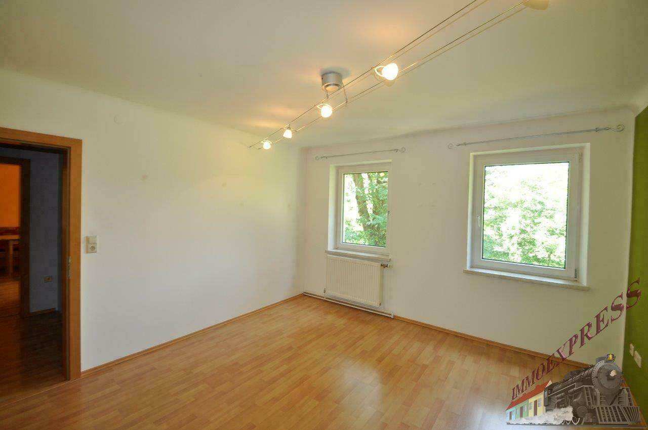 Geräumiges Wohnzimmer mit Holzparkettboden, weiß gestrichenen Wänden und natürlichem Lichteinfall.
