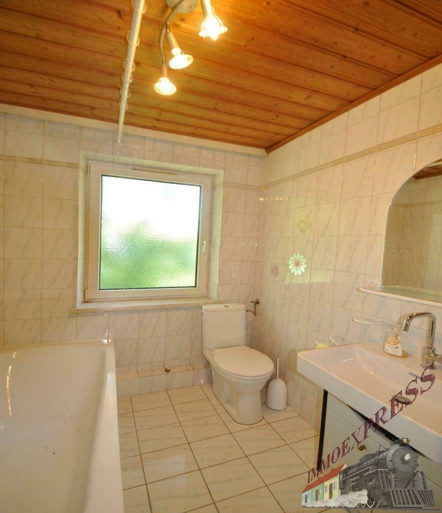 Badezimmer mit Badewanne, WC, Waschbecken, Fenster und Holzdeckenverkleidung.