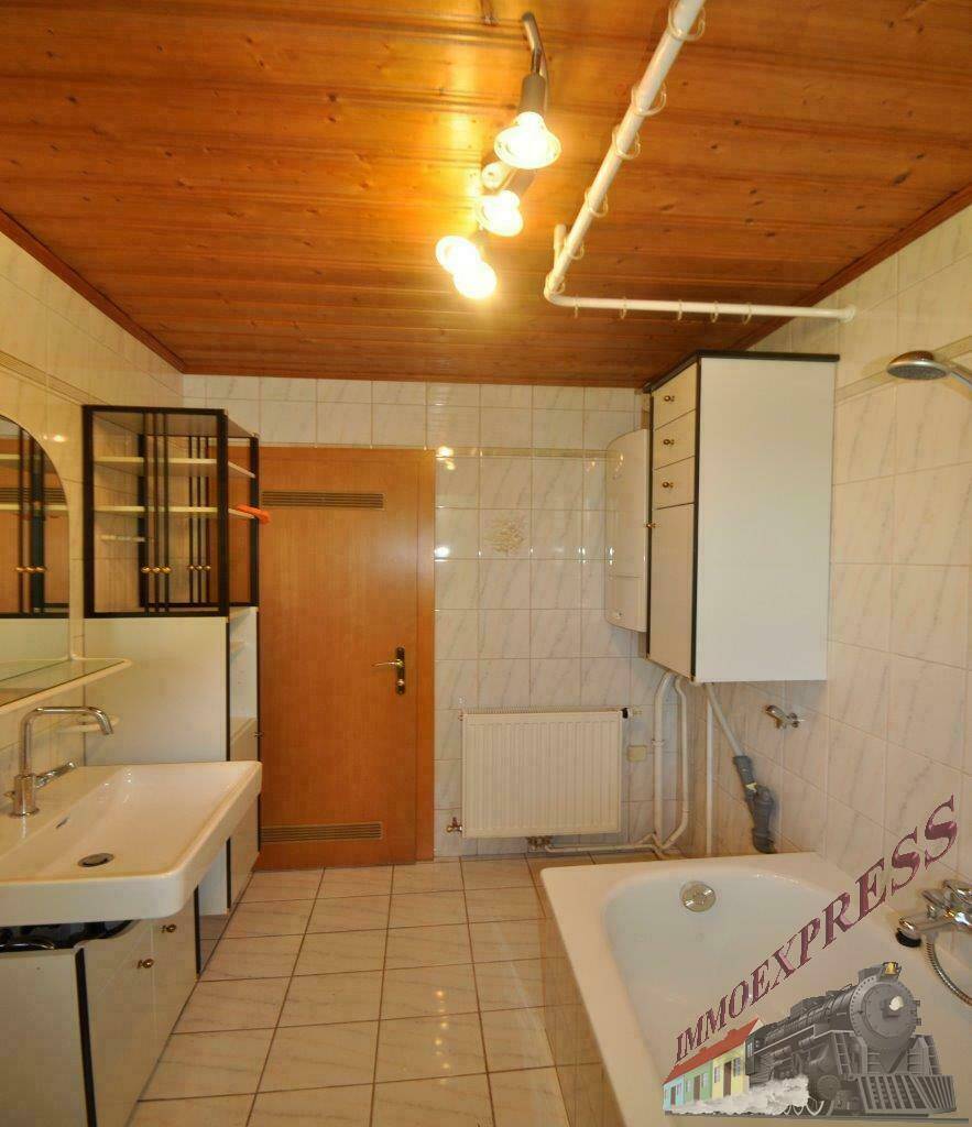 Gefliestes Badezimmer mit Badewanne, Waschbecken, Holzdecke und Duschvorrichtung.