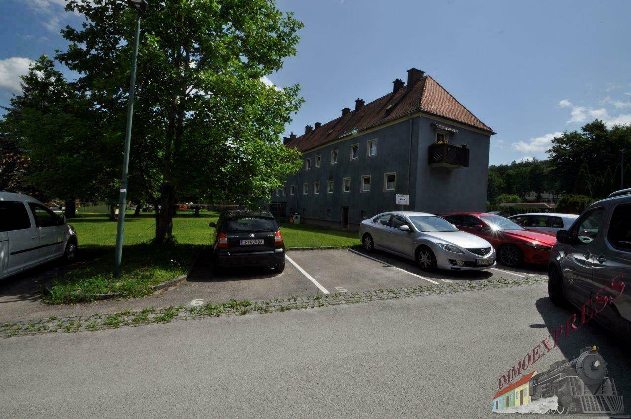 Mehrfamilienhaus mit Parkplätzen und Grünfläche im Freien.