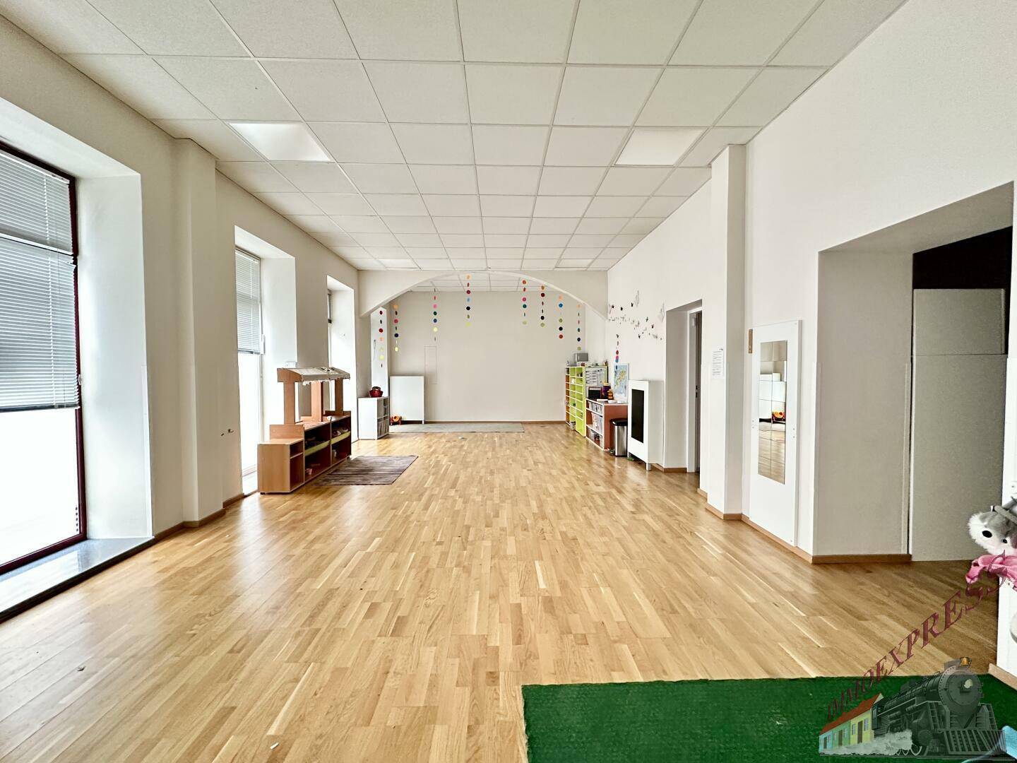 Geräumiger und heller Spielbereich mit Holzboden und weißen Wänden, bietet viel Platz für Aktivitäten.