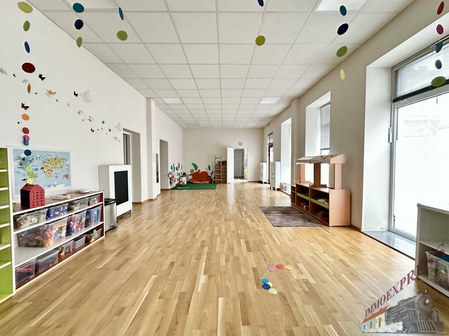 Weitläufiger Spielbereich mit Holzboden, bunten Dekorationen und viel Tageslicht, ideal für Kinderaktivitäten.
