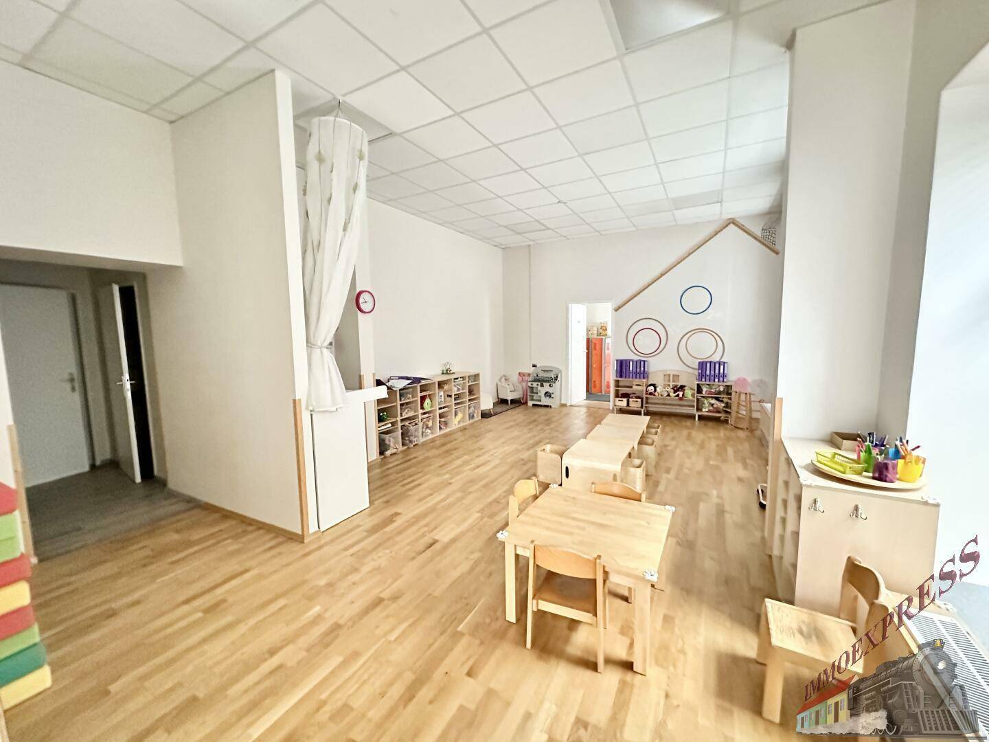Heller Spielraum mit Holzboden, kleinen Holztischen und einer Wickelstation, ideal für die Kinderbetreuung.