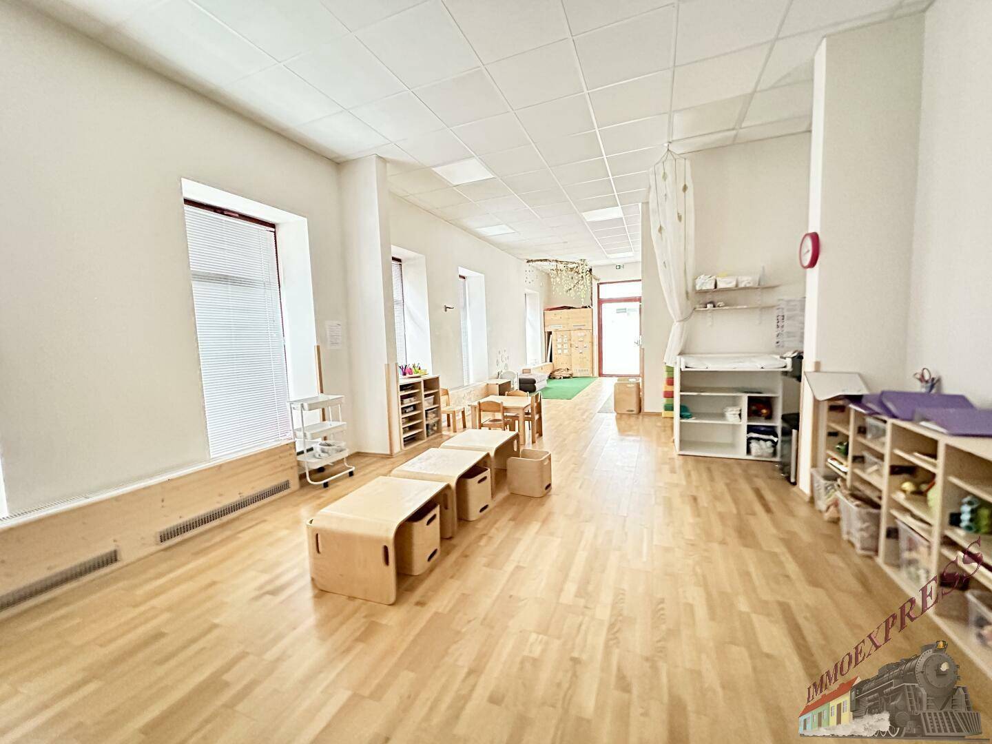 Langer, heller Spielraum mit Holzboden, niedrigen Holztischen und Regalen, ideal für eine Kindertagesstätte.