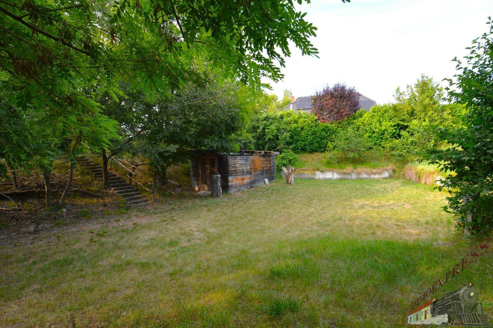 Großer Rasenbereich im Garten mit einem kleinen Holzschuppen und Treppen im Hintergrund.