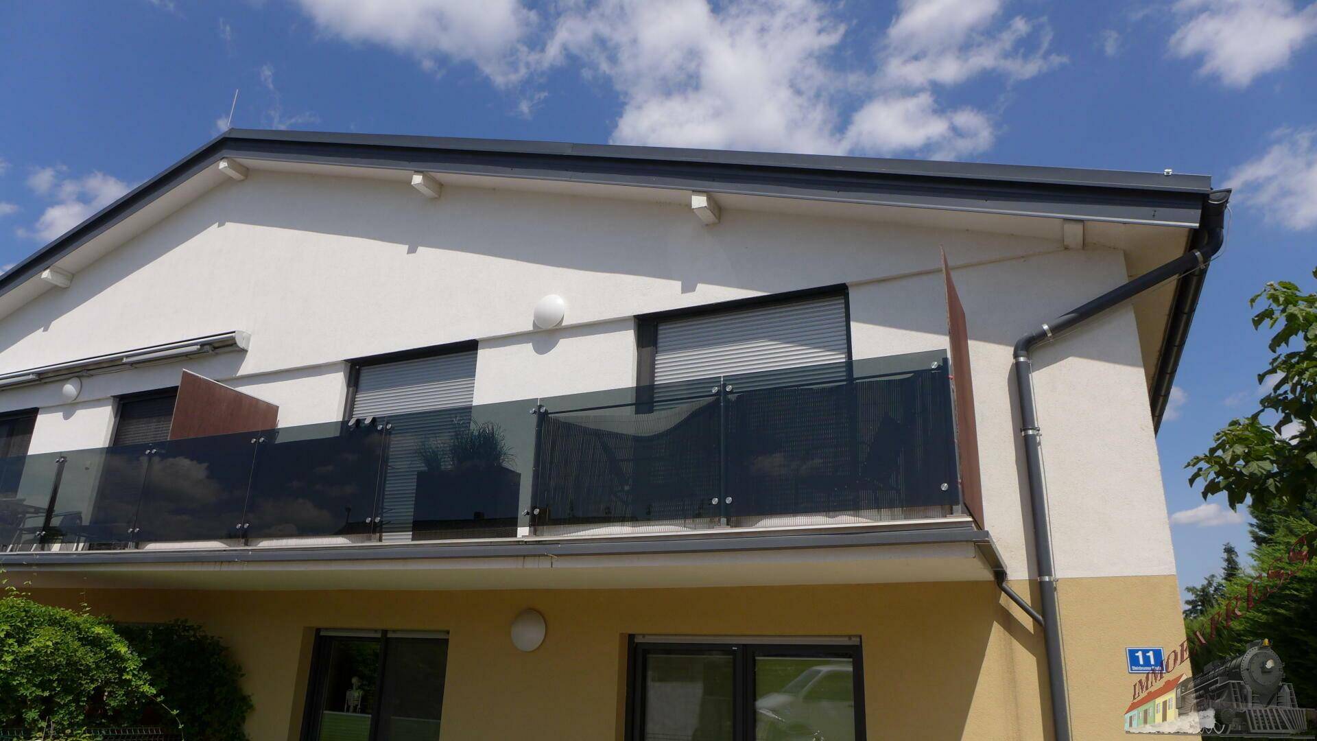 Moderne Gebäudefassade mit Balkonen, großen Fenstern und Rollläden unter blauem Himmel.
