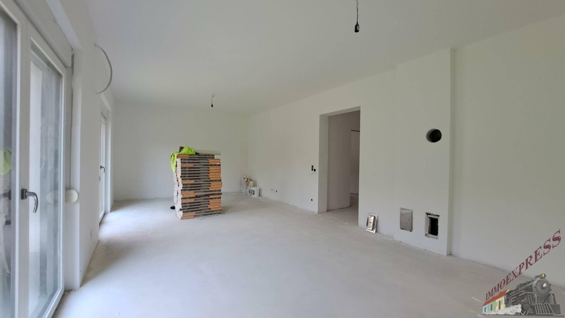 Geräumiger Wohnbereich im Rohbau mit großen Terrassentüren und Baumaterialien.