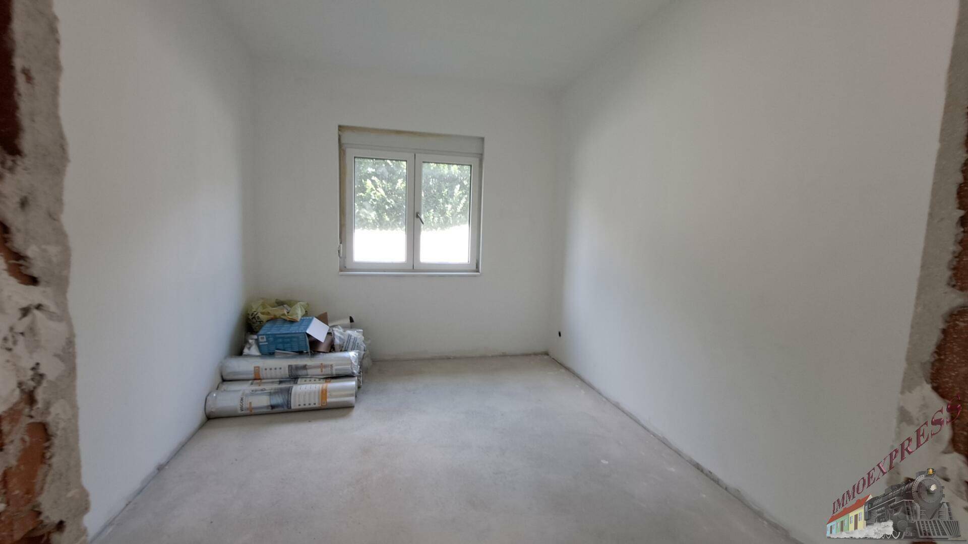 Schlafzimmer im Rohbau mit Fenster und gestapelten Baumaterialien.