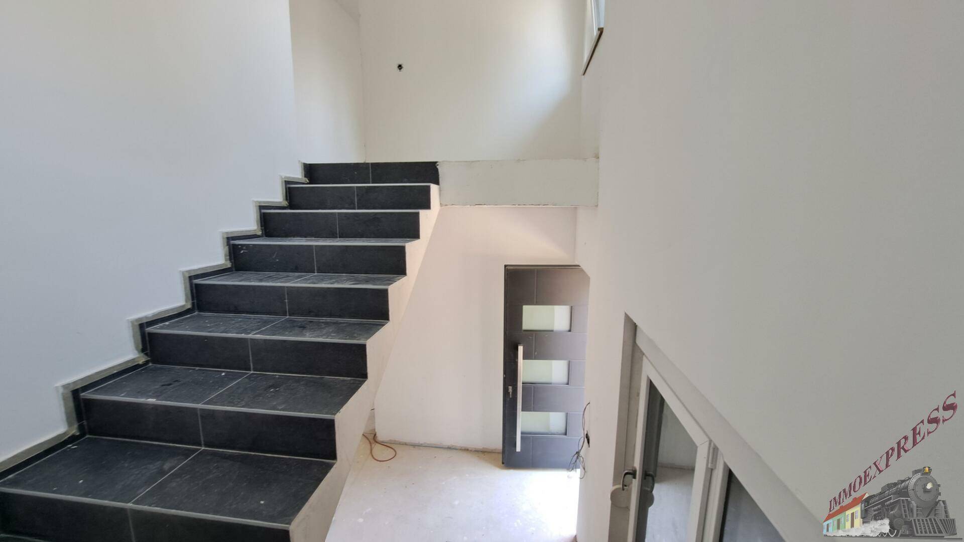 Treppenhaus mit dunklen Fliesenstufen und moderner Eingangstür.