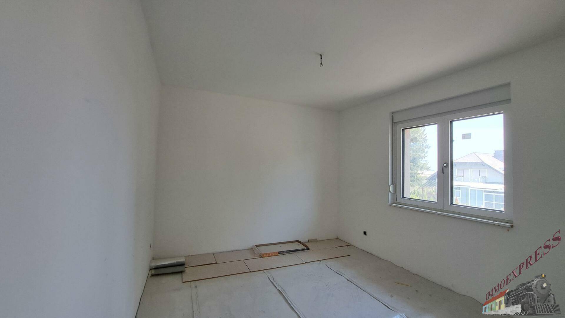 Schlafzimmer im Rohbau mit Fenster und gestapelten Bodenbelägen.