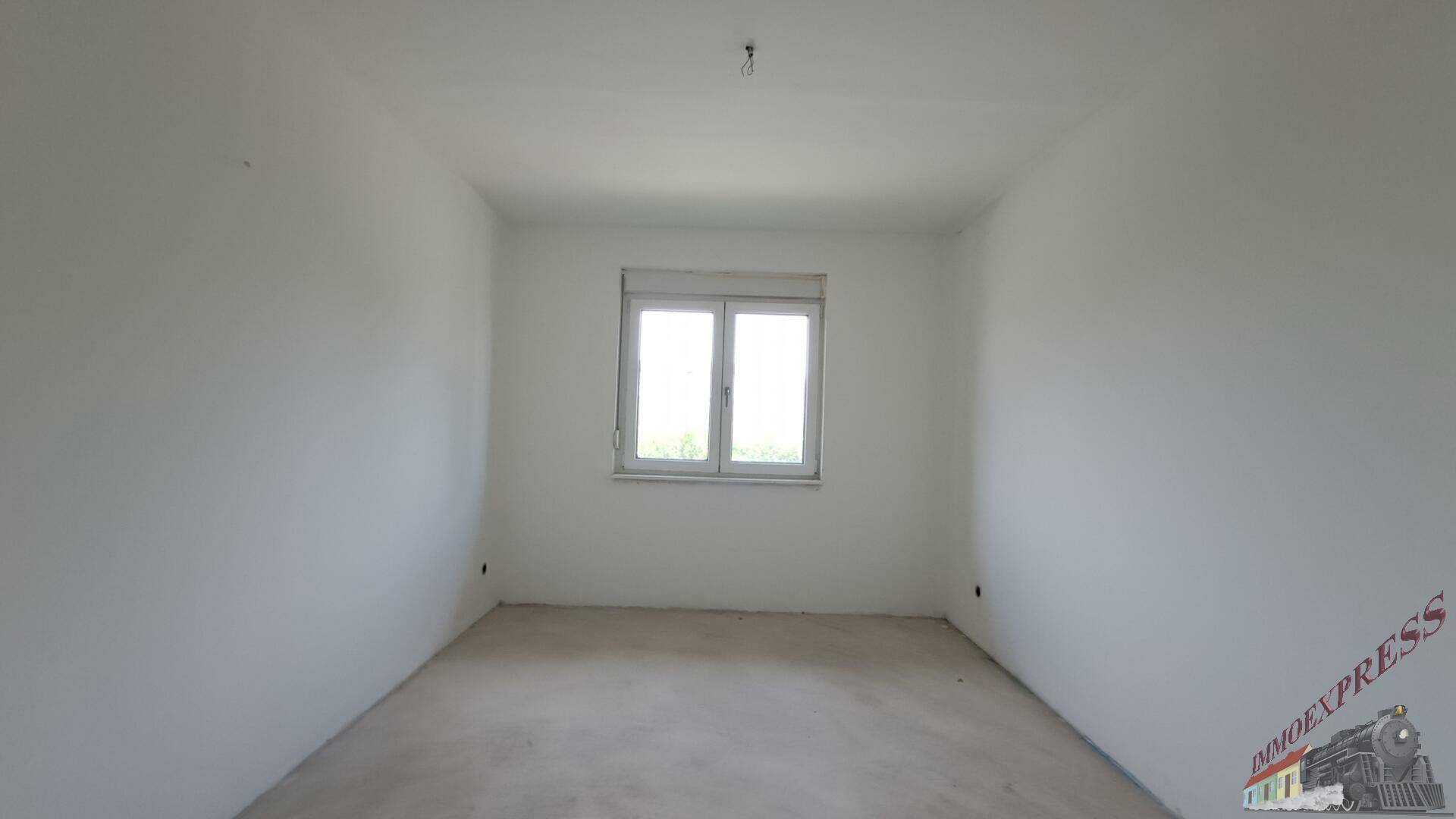 Helles Schlafzimmer im Rohbau mit einem Fenster und unfertigem Boden.