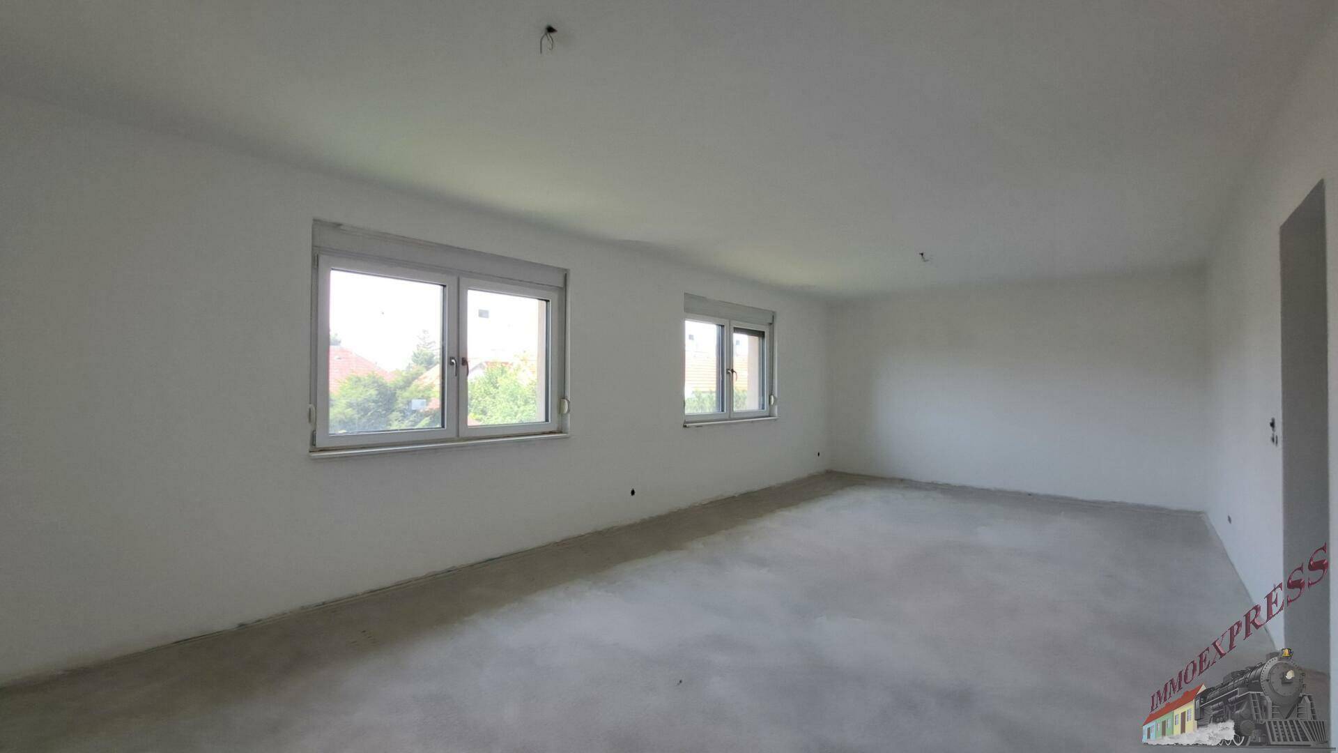 Weitläufiger Wohnbereich mit zwei Fenstern und unfertigem Estrichboden.