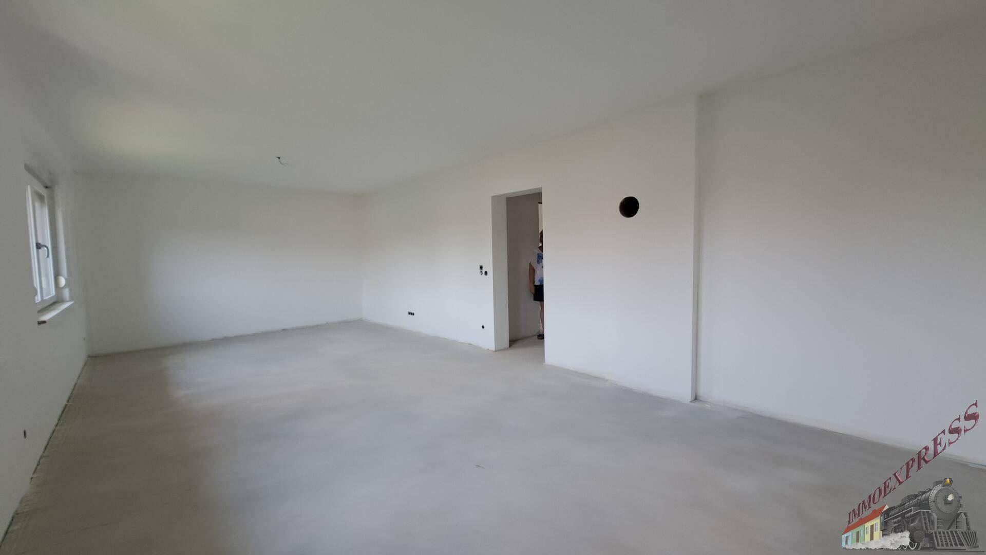 Heller Wohnraum im Neubau mit unfertigem Boden und weiß gestrichenen Wänden.