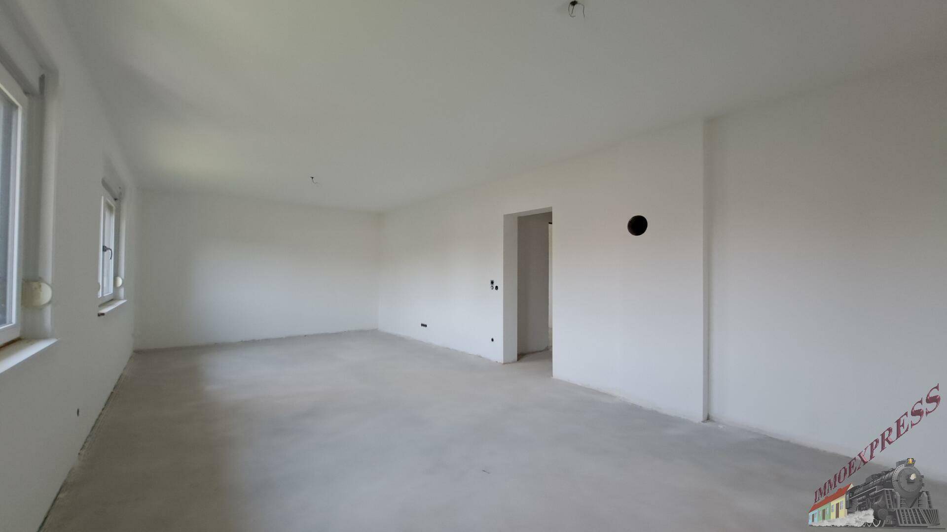 Geräumiger, heller Wohnbereich im Rohbauzustand mit großen Fenstern.