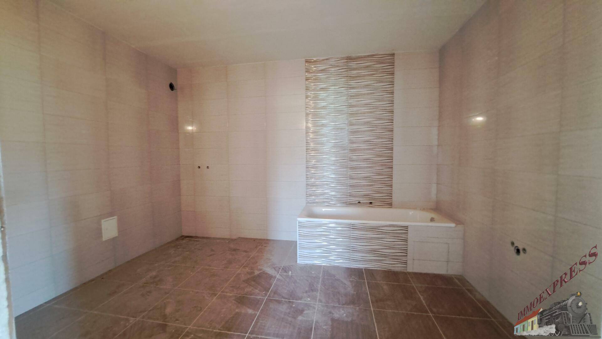 Modern gefliestes Badezimmer mit Badewanne und vorbereiteten Anschlüssen.