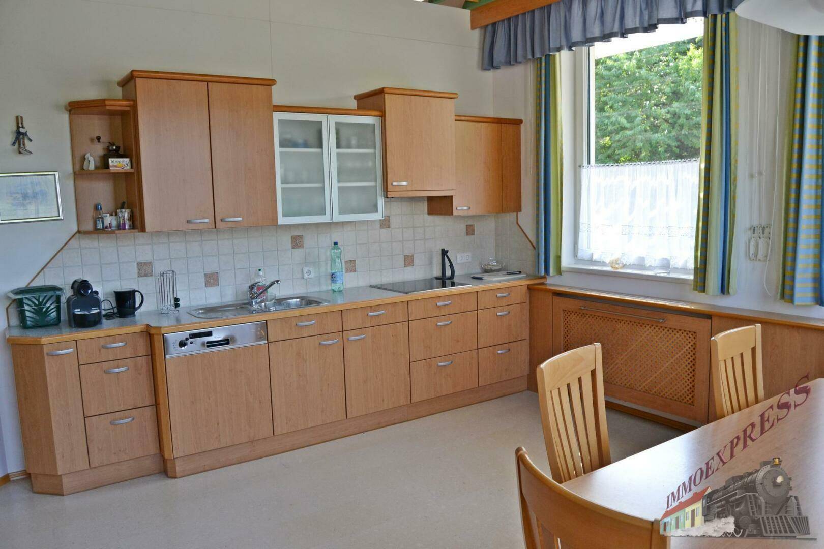 Funktionale Küche mit hellen Holzschränken, integriertem Geschirrspüler und Essbereich am Fenster.