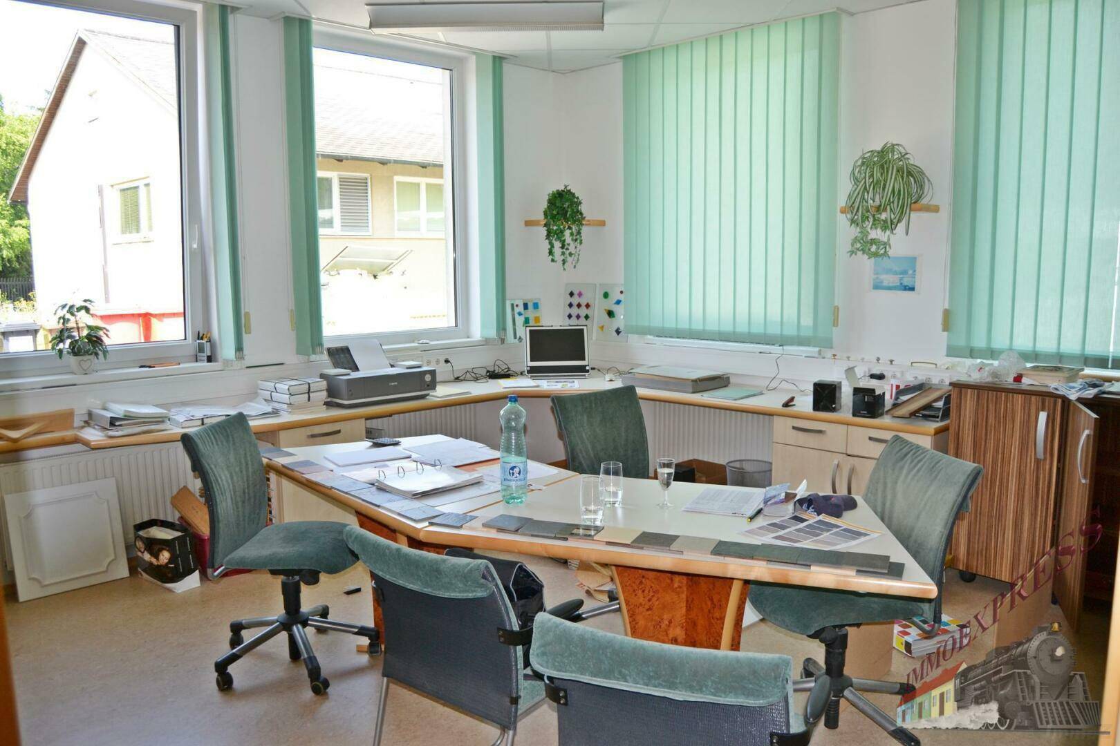 Helles Büro mit Eckschreibtisch, ergonomischen Stühlen und Blick ins Grüne durch große Fenster.