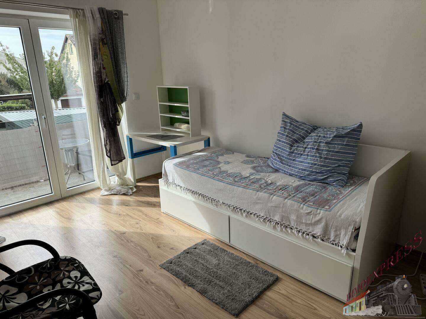 Helles Schlafzimmer mit Einzelbett, Schreibtisch und direktem Zugang zum Balkon.