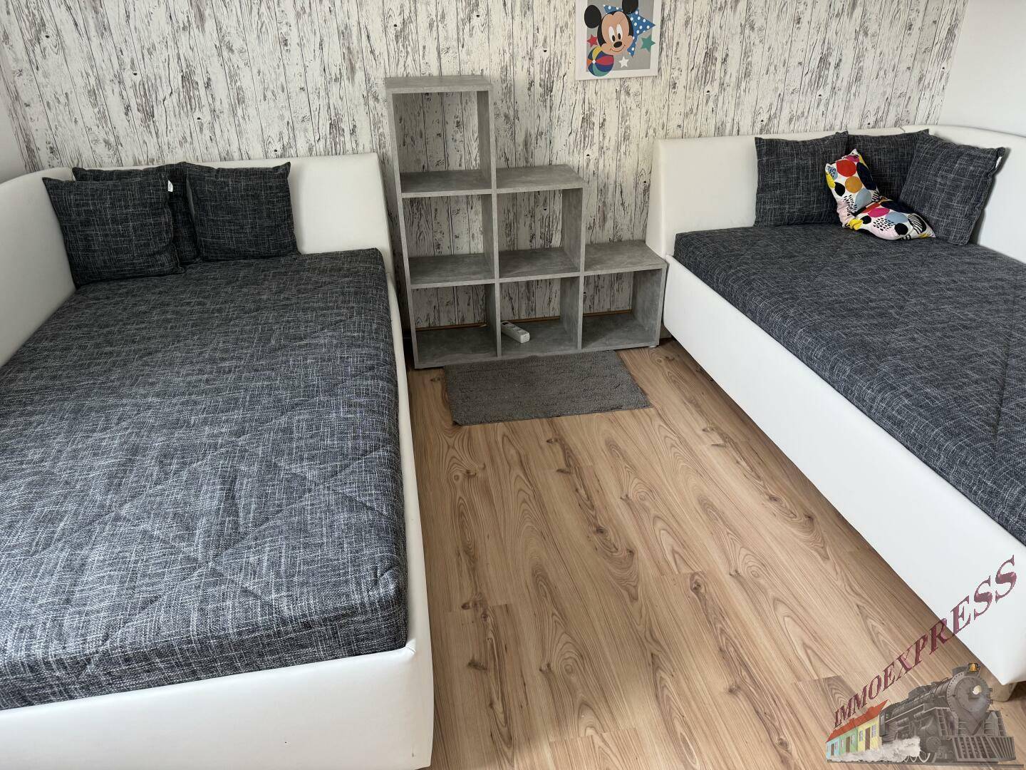 Kinderzimmer mit zwei Einzelbetten, Holzboden und verspielter Wanddekoration.