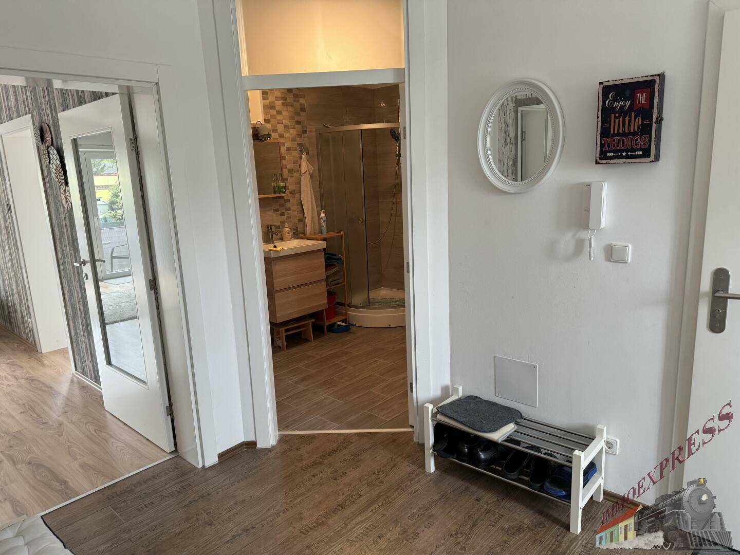 Flur mit Schuhregal und Blick in ein modernes Badezimmer mit Dusche.