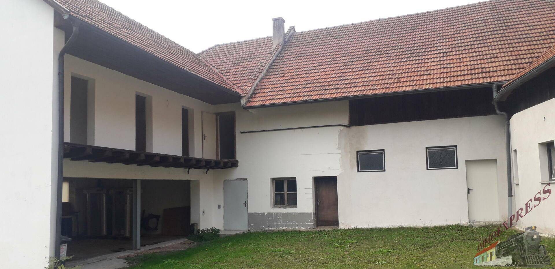 Rückseite eines ländlichen Gebäudes mit offenem Garagenbereich und rotem Ziegeldach.
