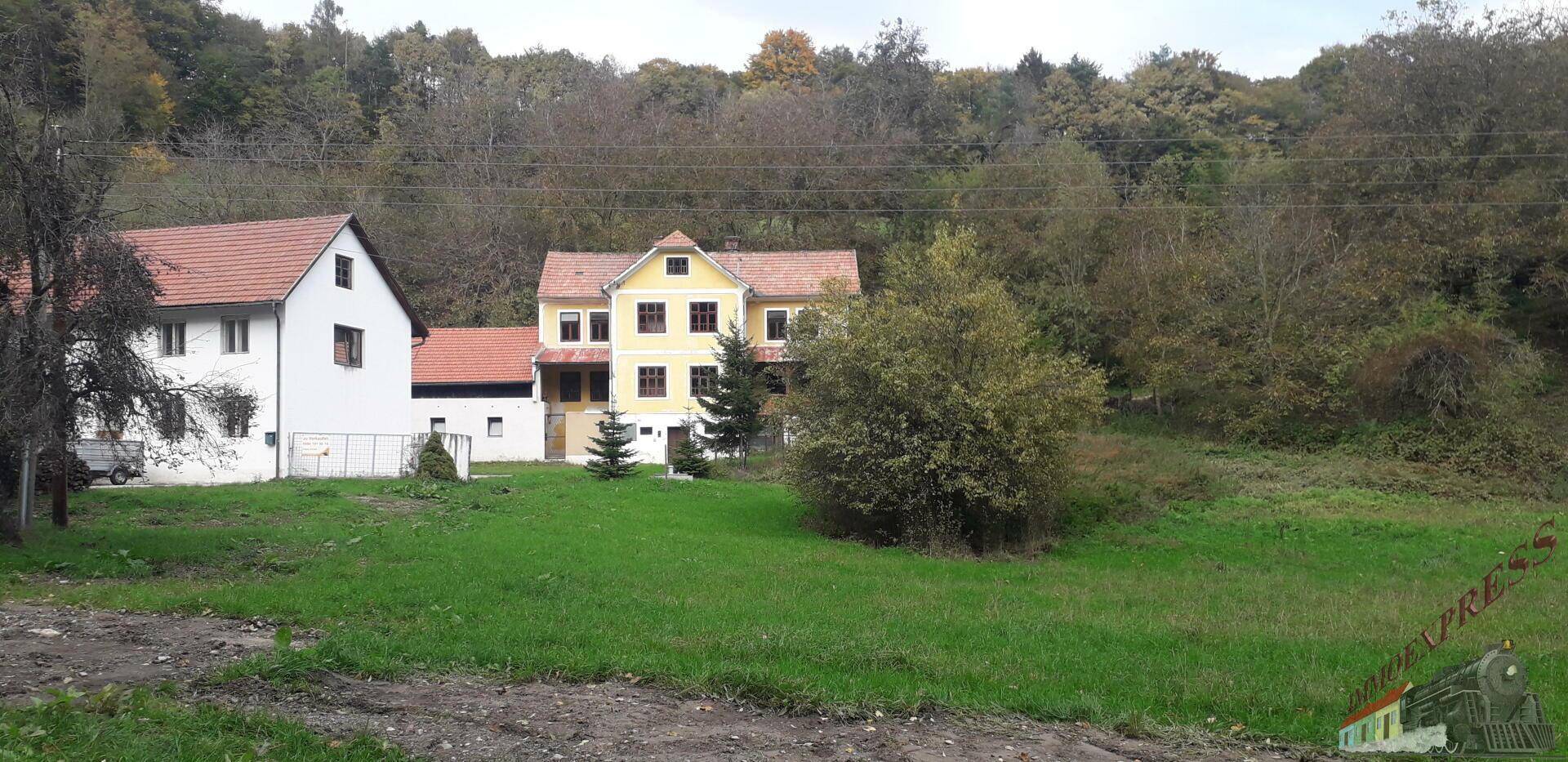 Zwei ländliche Gebäude mit roten Ziegeldächern, umgeben von grünen Wiesen und Bäumen.
